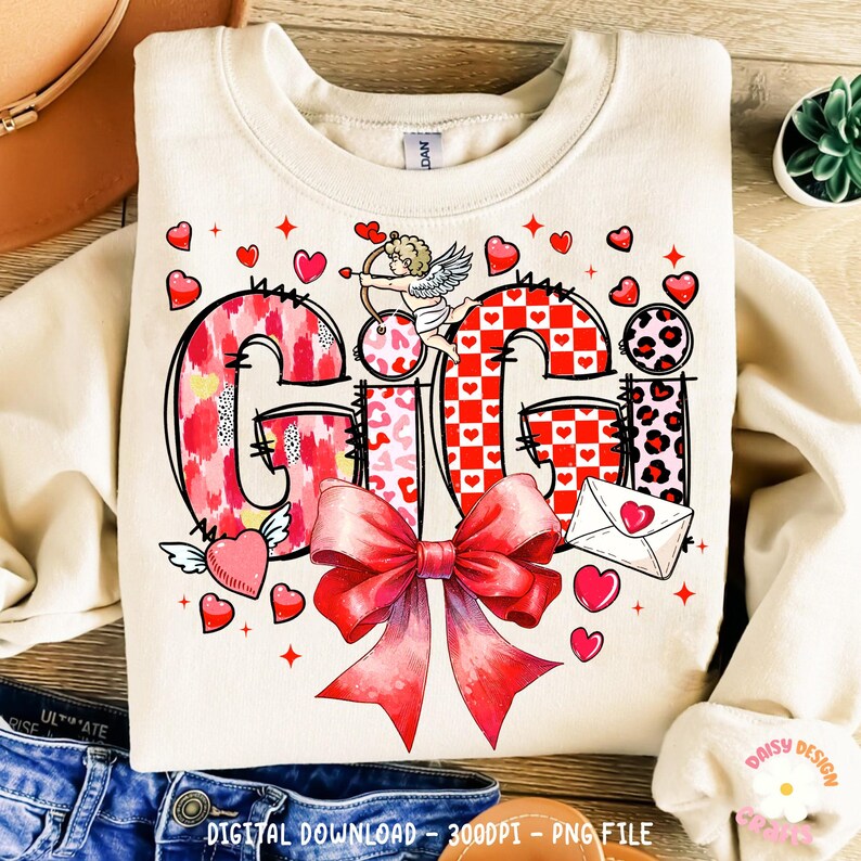 May include: A Valentine's Day design featuring the name "Gigi" in a patchwork style with hearts, bows, and a cupid. The design is on a cream-colored sweatshirt.