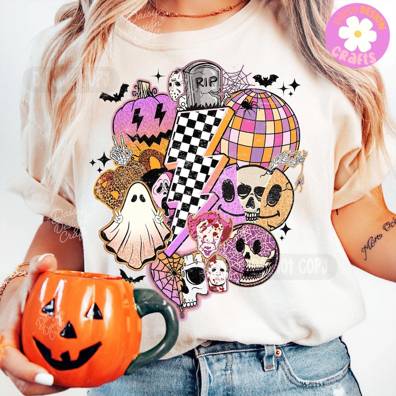 May include: Cream t-shirt with a Halloween graphic featuring a purple pumpkin, a checkered lightning bolt, a disco ball, skulls, and a ghost. An orange pumpkin mug is held in the foreground. The design is vibrant and festive.