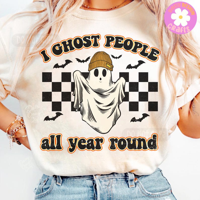 May include: Cream-coloured t-shirt featuring a ghost wearing a beanie and the text "I ghost people all year round." The design includes black bats and a checkered pattern, suitable for Halloween or general wear.