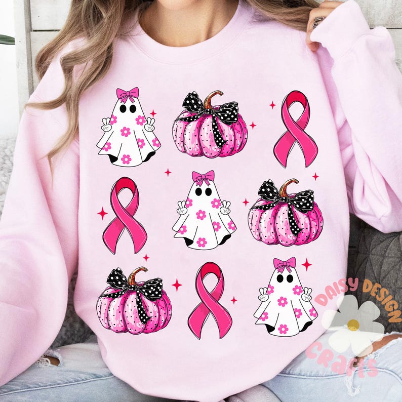 May include: Pink sweatshirt with a pattern of pink pumpkins, ghosts, and pink ribbons. The pumpkins have black polka dots and black bows. The ghosts have white flowers and pink bows. The ribbons are in the shape of awareness ribbons.