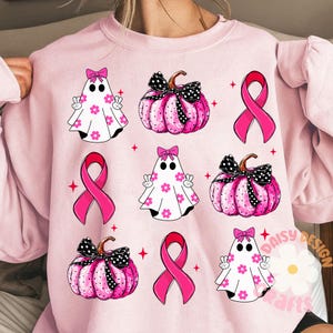 May include: Pink sweatshirt with a pattern of pink pumpkins, ghosts, and pink ribbons. The text "Daisy Design Crafts" is in the bottom right corner.