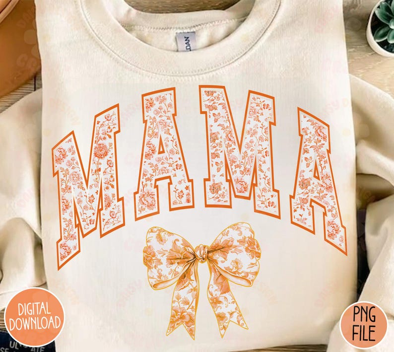 May include: A white sweatshirt with the word "MAMA" in orange letters with a floral pattern. A large orange bow with a floral pattern is below the word.
