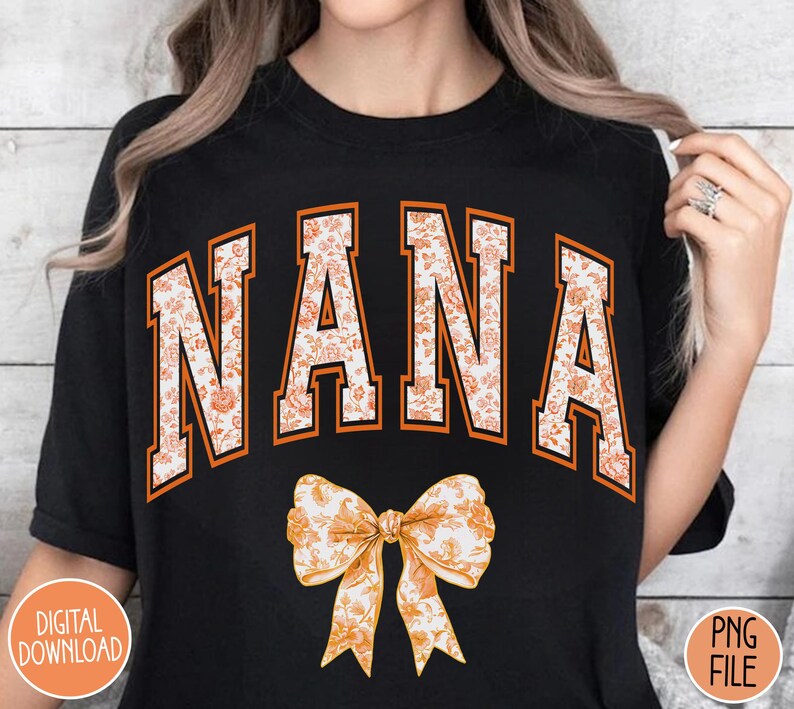 May include: Black t-shirt with the word "NANA" in orange letters with a floral pattern. The word is in a collegiate font style. A floral bow is below the word.