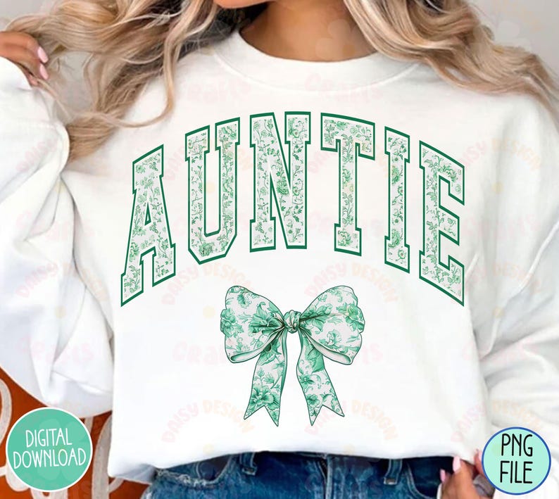 May include: White sweatshirt with the word "AUNTIE" in green letters with a floral pattern. A green floral bow is below the text.