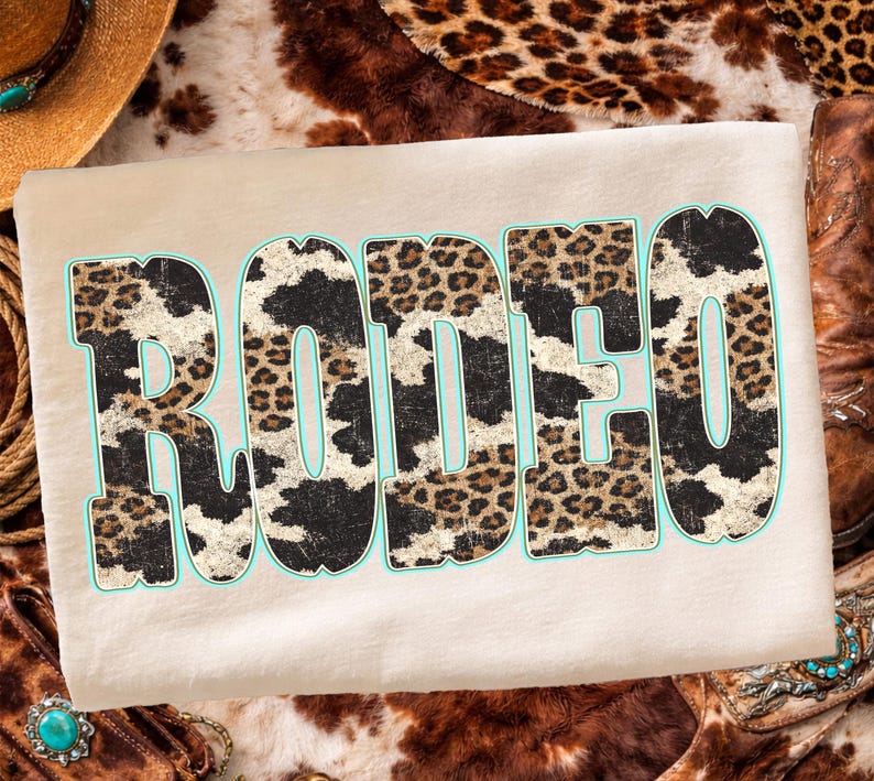 Pu&ograve; includere: Una maglietta beige con la scritta "RODEO" in grandi lettere consumate. Le lettere sono riempite con un motivo a stampa di pelle di mucca e leopardo, delineate in azzurro. La maglietta ha un tema western.