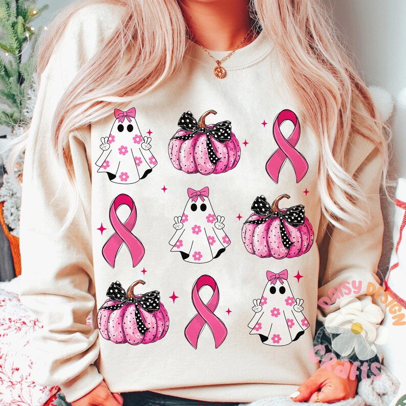 May include: A white sweatshirt with a pink and black pattern of pumpkins, ghosts, and pink ribbons. The design is a cute and festive way to show support for breast cancer awareness.