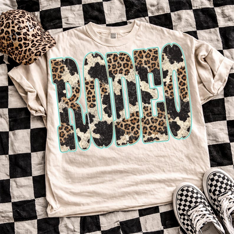 Pu&ograve; includere: Una maglietta beige con la scritta "RODEO" in un audace design animalier con un contorno azzurro. Sono visibili anche un cappello a secchiello con stampa leopardata abbinato e scarpe da ginnastica a scacchi.