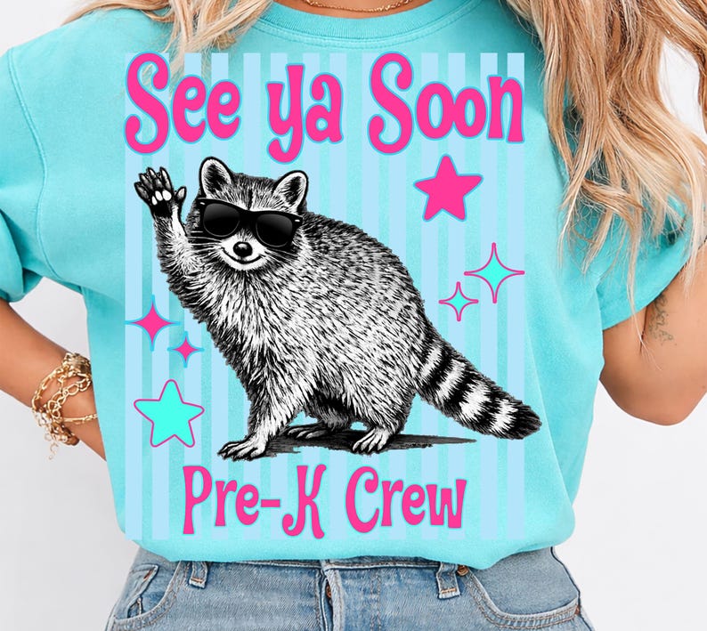 Op de afbeelding: Een lichtblauw T-shirt met de tekst "See ya Soon Pre-K Crew". Het shirt heeft een cartoon wasbeer met een zonnebril die zwaait. Roze sterren en blauwe sterrenhemels versieren het shirt.