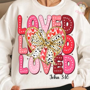 May include: White sweatshirt with a pink, red and white graphic design that says "Loved Loved Loved" with a gold bow and hearts. The text "John 3:16" is printed below the graphic.