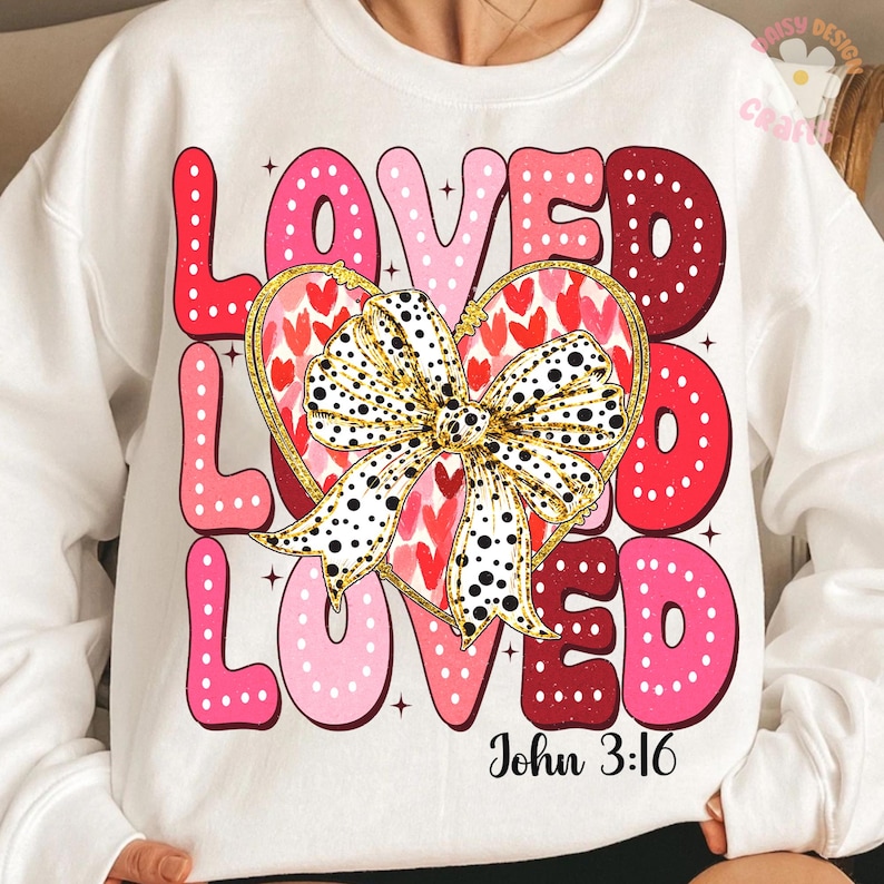 May include: White sweatshirt with a pink, red and white graphic design that says "Loved Loved Loved" with a gold bow and hearts. The text "John 3:16" is printed below the graphic.
