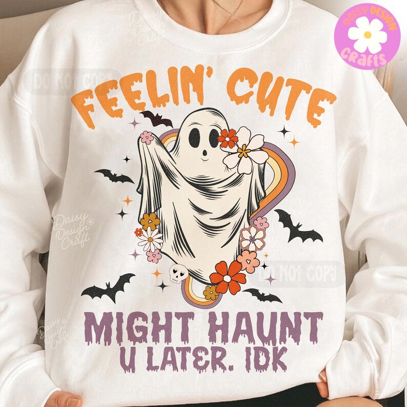 May include: White sweatshirt featuring a ghost design with flowers and a rainbow. The text reads "FEELIN' CUTE" and "MIGHT HAUNT U LATER. IDK". The design includes black bats and stars, creating a fun, spooky aesthetic.