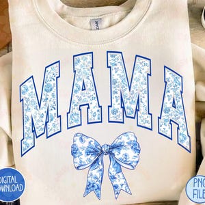 May include: A white sweatshirt with the word "MAMA" in blue letters with a blue and white floral pattern. A blue and white floral bow is below the word.