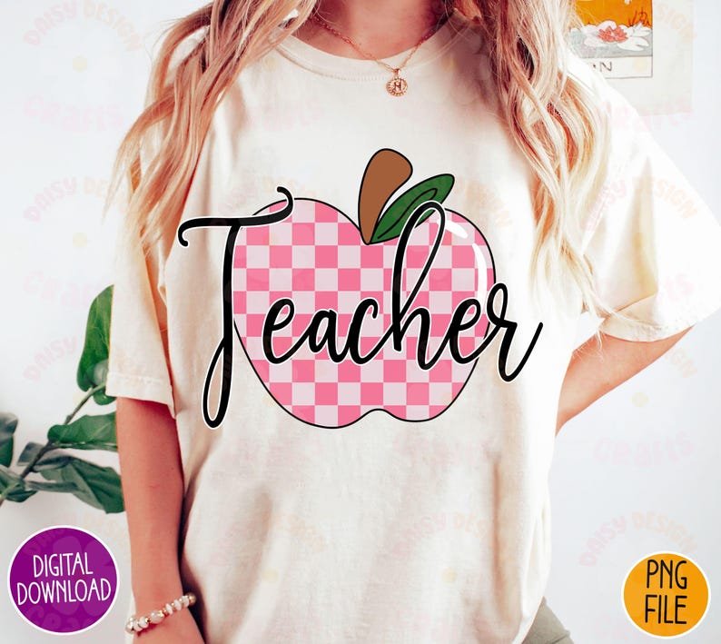 K&ouml;nnte beinhalten: Ein wei&szlig;es T-Shirt mit einem pink-wei&szlig; karierten Apfel-Design und dem Wort "Teacher" in schwarzer Schrift.