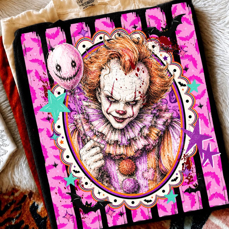 May include: A black t-shirt featuring a graphic print of a clown with orange hair, a ruffled collar, and a pink balloon. The design is framed by a scalloped oval border against a background of black vertical stripes, pink bats, and stars.