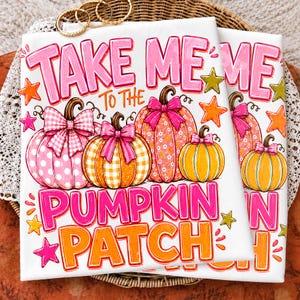 May include: A white t-shirt featuring the text "TAKE ME TO THE PUMPKIN PATCH" in pink and orange. The design includes four illustrated pumpkins in shades of pink and orange, each adorned with a decorative bow, surrounded by colorful stars.