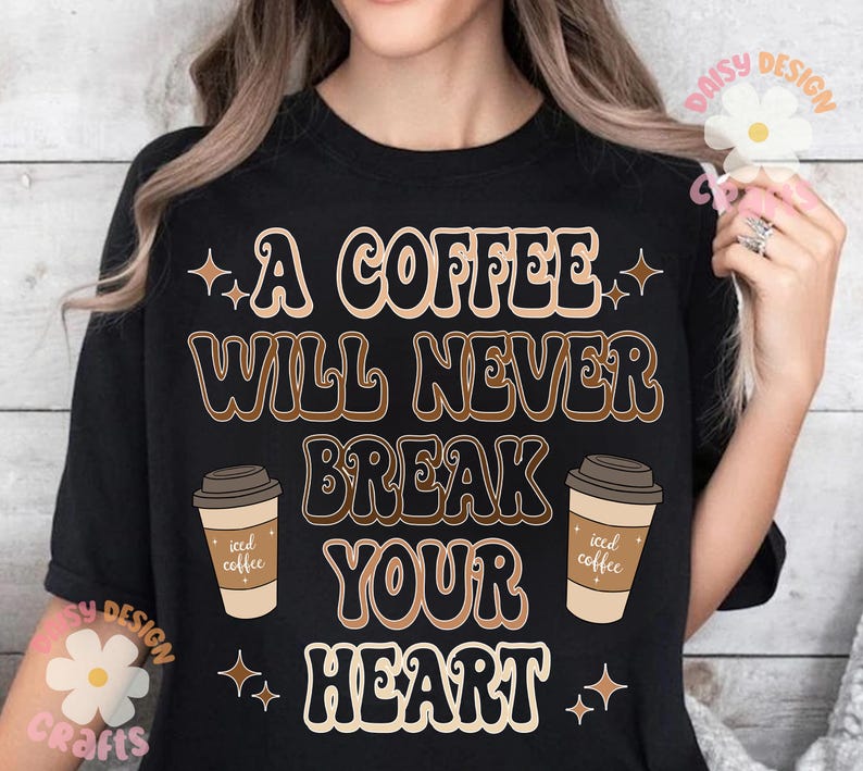 Puede incluir: Camiseta negra con un gr&aacute;fico de estilo retro que dice "Un caf&eacute; nunca romper&aacute; tu coraz&oacute;n". El gr&aacute;fico presenta dos tazas de caf&eacute; helado.