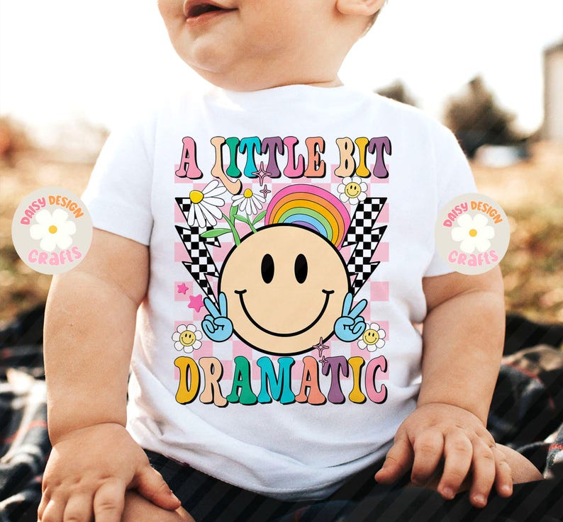 Op de afbeelding: Een wit T-shirt met een regenboog, een smiley en de tekst "A little bit dramatic" in kleurrijke letters.