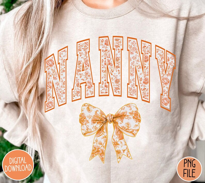 May include: A white sweatshirt with the word "NANNY" in orange letters with a floral pattern. The letters are outlined in orange. A large orange bow with a floral pattern is below the word.