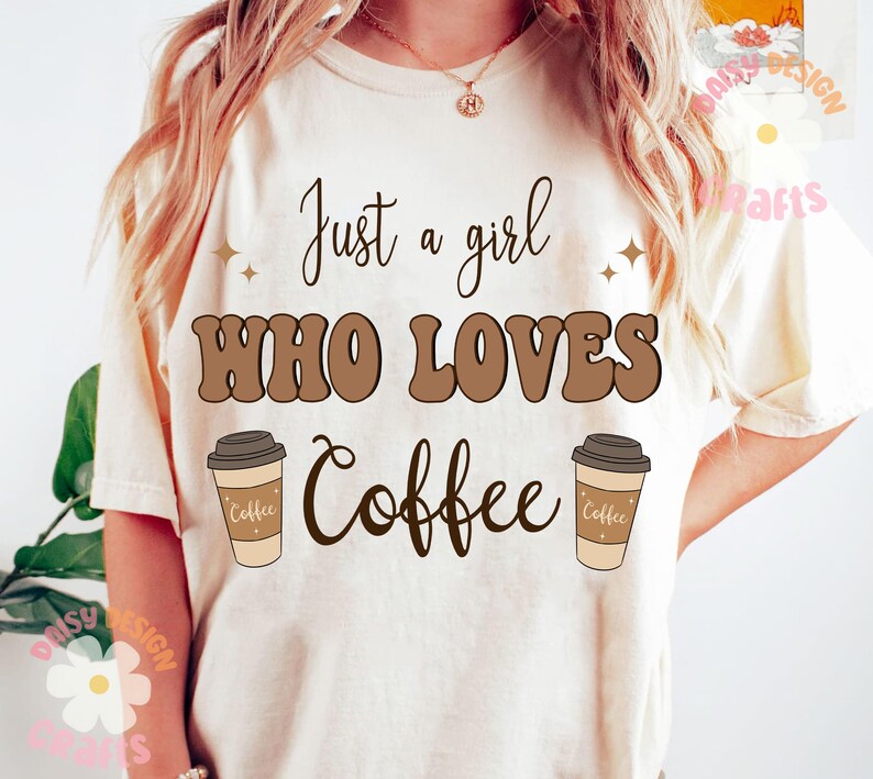 Puede incluir: Una camiseta blanca con el texto "Just a girl who loves coffee" en letras marrones. Dos tazas de caf&eacute; marrones con la palabra "coffee" en ellas est&aacute;n a cada lado del texto.