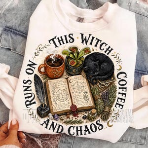 Puede incluir: Una sudadera blanca con un estampado gráfico de una taza de café humeante, una venus atrapamoscas, un gato negro dormido, un libro de hechizos abierto con diagramas, una pluma, cristales y hierbas, con el texto THIS WITCH RUNS ON COFFEE AND CHAOS.