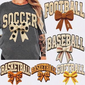May include: A dark gray t-shirt with the word "SOCCER" in cream-colored block letters and a black and cream-colored bow. Additional images show "FOOTBALL", "BASEBALL", "BASKETBALL", and "SOFTBALL" designs.