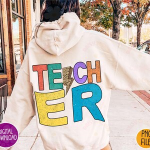 K&ouml;nnte beinhalten: Ein wei&szlig;er Hoodie mit dem Wort "TEACHER" auf der R&uuml;ckseite in bunten Buchstaben mit einem Leopardenmuster und einem Blitz.