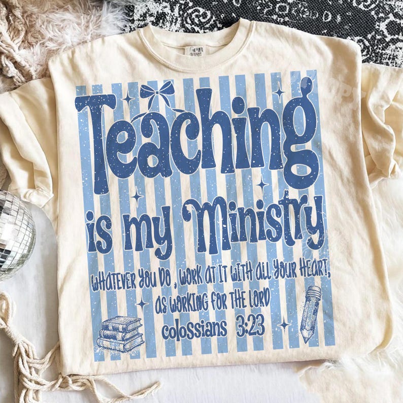 Puede incluir: Una camiseta de color crema con un fondo de rayas verticales azules y el texto "Teaching is my Ministry" en una fuente grande y negrita. Debajo, se lee "Whatever you do, work at it with all your heart, as working for the Lord, Colossians 3:23", acompa&ntilde;ado de una pila de libros y un gr&aacute;fico de un l&aacute;piz.