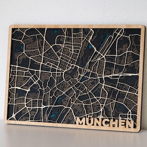 Puede incluir: Un mapa de madera de Múnich, Alemania, con fondo negro y líneas blancas que representan las calles. El nombre de la ciudad "MÜNCHEN" está impreso en blanco en la parte inferior del mapa.