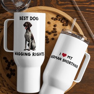 May include: Two white travel mugs with handles and lids. One mug has a graphic of a German Shorthair Pointer and the text "BEST DOG WAGGING RIGHTS". The other mug says "I ❤️ MY GERMAN SHORTHAIR".