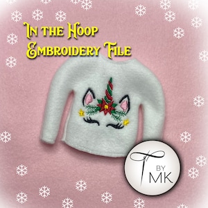 May include: White elf-sized sweater with a unicorn embroidered on the front. The unicorn has a red poinsettia, green holly, and gold stars. The text "In the Hoop Embroidery File" is at the top of the image. The text "By MK" is in a circle with a needle and thread.