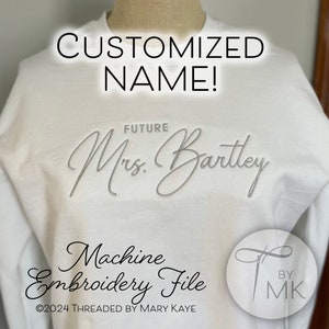 May include: White sweatshirt with the text "CUSTOMIZED NAME!" and "FUTURE Mrs. Bartley" embroidered in silver thread. The bottom of the sweatshirt has the text "Machine Embroidery File ©2024 THREADED BY MARY KAYE" and a logo with the text "BY MK".