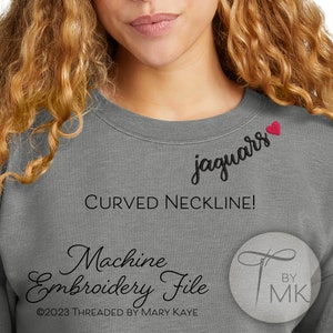 May include: A gray sweatshirt with a curved neckline and a small red heart embroidered on the neckline. The text "jaguars" is embroidered in black cursive lettering. The text "Machine Embroidery File" is written in black cursive lettering below the neckline. The text "©2023 THREADED BY MARY KAYE" is written in black lettering below the embroidery file text. The text "BY MK" is written in black lettering in a stylized font.