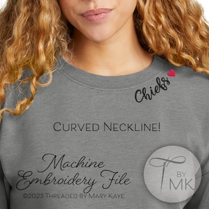 May include: Gray sweatshirt with a curved neckline and a small red heart embroidered on the right shoulder. The text "Chiefs" is embroidered in black below the heart. The text "Machine Embroidery File" is written in cursive below the neckline. The text "©2023 Threaded by Mary Kaye" is written in black below the embroidery file text. The text "BY MK" is written in black in a circle with a needle and thread design.