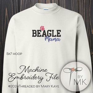 Puede incluir: Sudadera blanca con un diseño bordado en negro y morado que dice "BEAGLE Mama" con una huella de pata rosa sobre el texto. El texto "5x7 HOOP" está en la esquina inferior izquierda. El texto "Machine Embroidery File" está en cursiva debajo del diseño. El texto "©2024 THREADED BY MARY KAYE" está debajo de la cursiva. Un círculo con una aguja e hilo y una flor está en la esquina inferior derecha con el texto "BY MK" en el círculo.