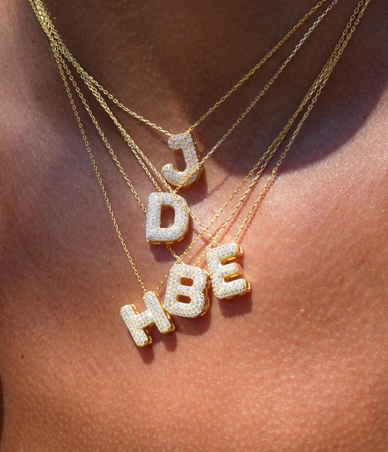 Puede incluir: Un conjunto de collares de oro con colgantes de letras engastados con diamantes. Las letras son J, D, H, B y E.