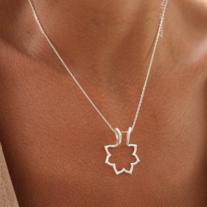 May include: A silver necklace featuring a pendant with an open, eight-pointed star design. The delicate chain hangs against a person's skin, with the pendant resting near the collarbone. The necklace is a simple, elegant piece of jewelry.