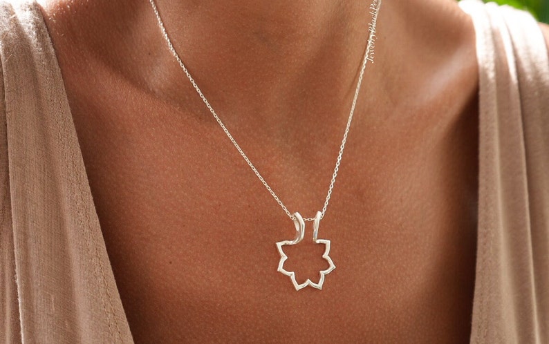 May include: A silver necklace featuring a pendant with an open, eight-pointed star design. The delicate chain hangs against a person's skin, with the pendant resting near the collarbone. The necklace is a simple, elegant piece of jewelry.