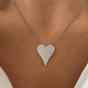May include: A silver necklace with a large, heart-shaped pendant covered in small, clear cubic zirconia stones.
