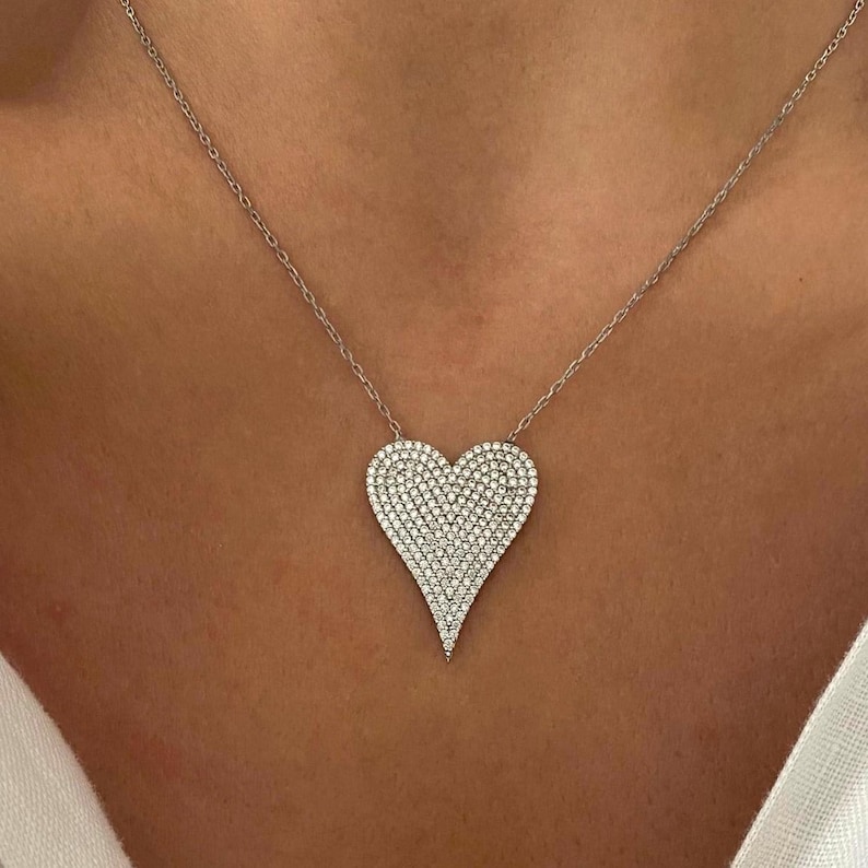 May include: A silver necklace with a large, heart-shaped pendant covered in small, clear cubic zirconia stones.