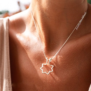 May include: A silver necklace with a geometric pendant in the shape of an eight-pointed star. The necklace is worn on a person with fair skin, and the chain is delicate. The text "JewelryBlackPearl" is visible on the chain.