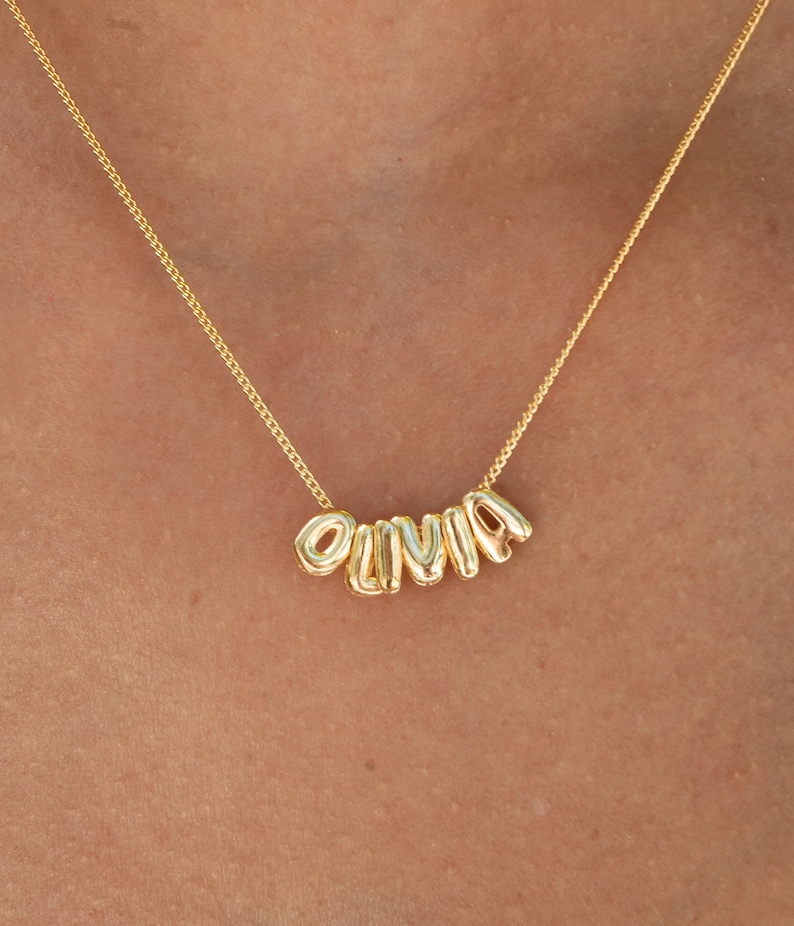 May include: A gold chain necklace with the name "Olivia" spelled out in gold letters.