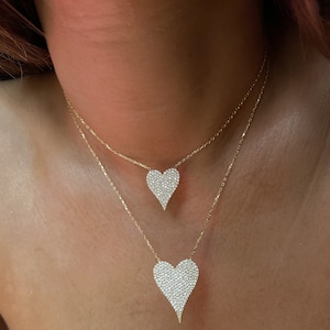 May include: A gold chain necklace with two heart-shaped pendants. Both pendants are covered in small, clear crystals.