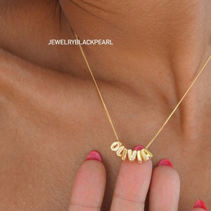 May include: Gold necklace with the name "Olivia" spelled out in individual letter charms.