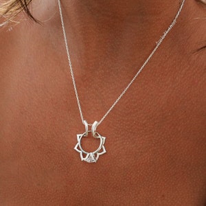 May include: A silver necklace with a pendant featuring a floral design and a central gemstone. The necklace is displayed against a skin tone background, highlighting the delicate chain and pendant details. The pendant has a flower-like shape.
