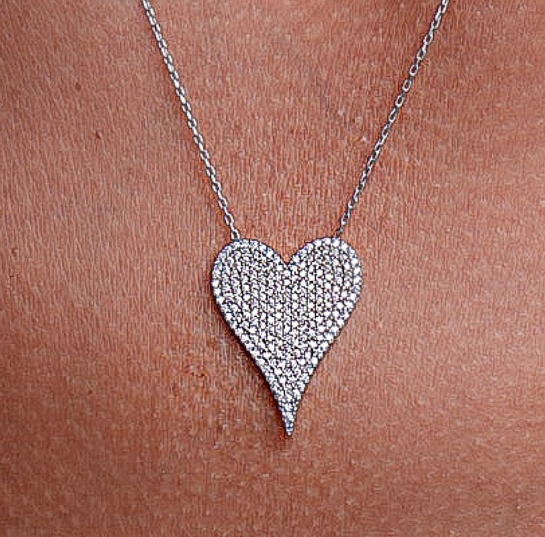May include: A silver chain necklace with a large, heart-shaped pendant covered in small, clear cubic zirconia stones.
