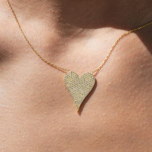 May include: A gold chain necklace with a large, heart-shaped pendant covered in small, sparkling stones.