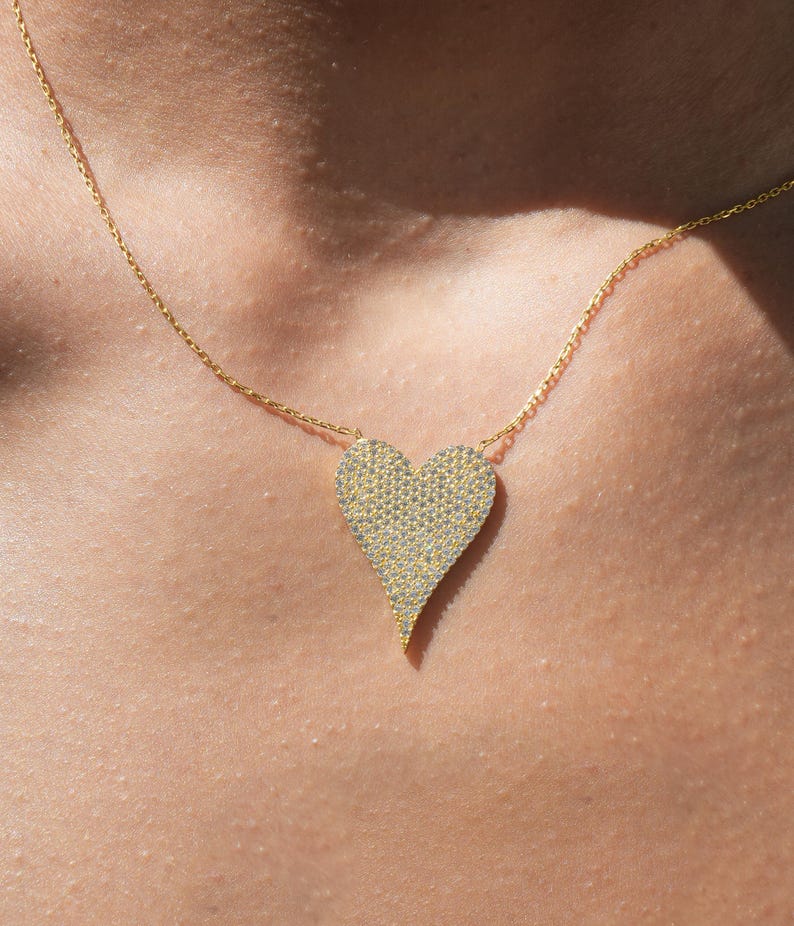 May include: A gold chain necklace with a large, heart-shaped pendant covered in small, sparkling stones.