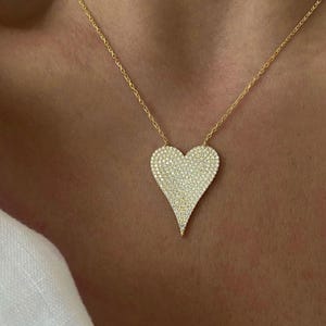 May include: A gold chain necklace with a large, heart-shaped pendant covered in sparkling clear stones.