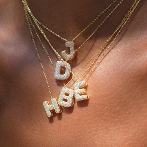 Puede incluir: Un conjunto de collares de oro con letras engastadas con diamantes que deletrean "HBE" y "J".