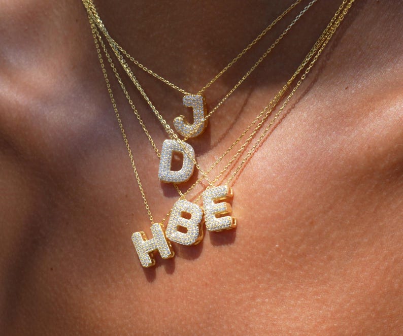 Puede incluir: Un conjunto de collares de oro con letras engastadas con diamantes que deletrean "HBE" y "J".